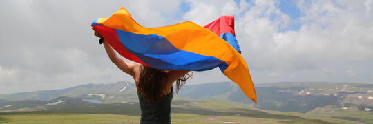 Woman holding Armenian flag overlooking land.