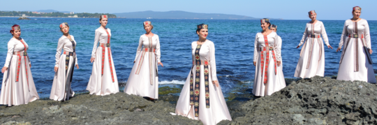 Plovdiv dancers in traditional costumes posing together by an open ocean and clear blue sky
