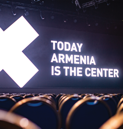Conference chairs in bottom of frame, with screen in background as focal point with text "Today Armenia is the Center."