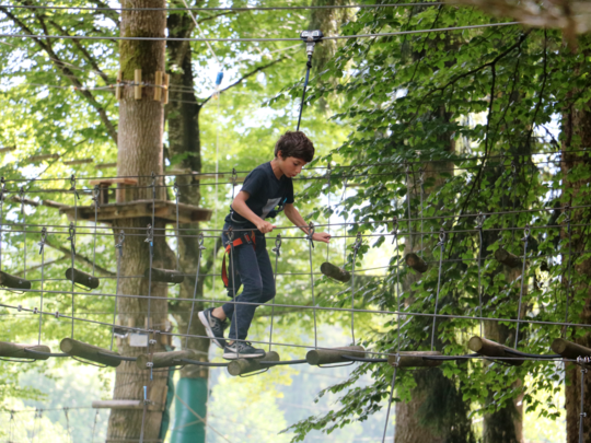 Young camper walks on a plank bridge suspended above the ground.