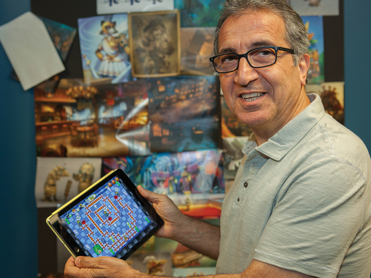 A man with glasses staring at the camera, showing the game he developed on a tablet in his hand.