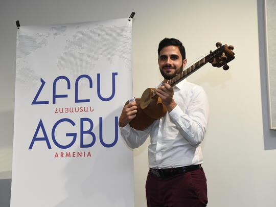MAP participant standing in front of AGBU poster with his kamancha